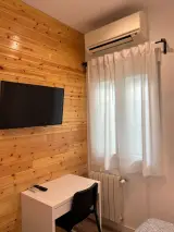 Ventana con cortinas blancas bajo el aire acondicionado, con escritorio y radiador en la habitación